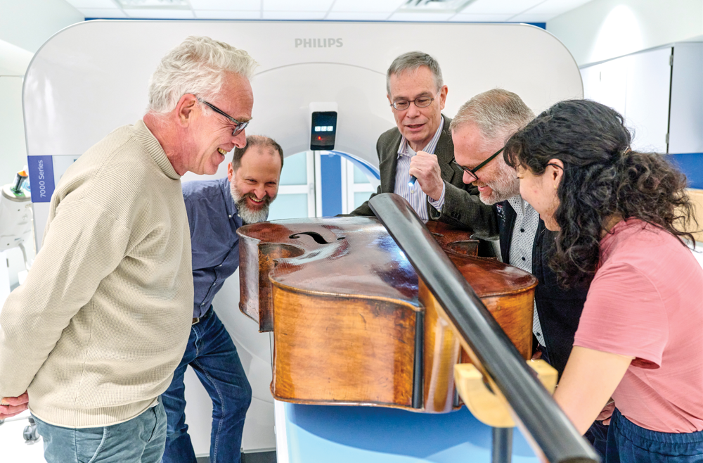 Members of the instrument imaging team stand on either side of a double bass that lays on a table in front of a CT machine.